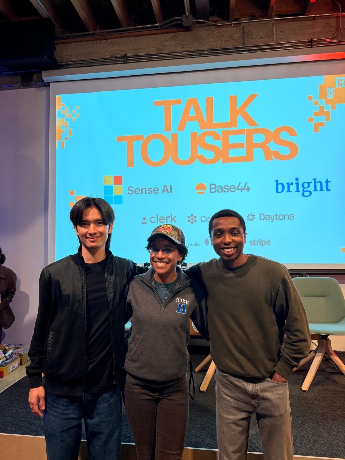 Three people standing in front of a Talk to Users event screen